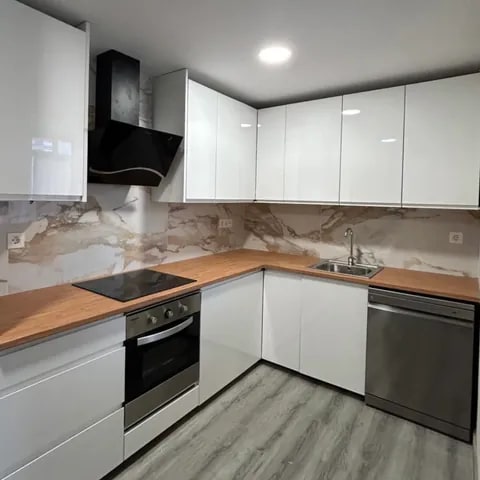 Cocina en L con mobiliario de carpintería blanco y encimera efecto madera