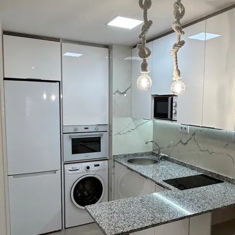 Cocina compacta con mobiliario de carpintería blanco y electrodomésticos integrados