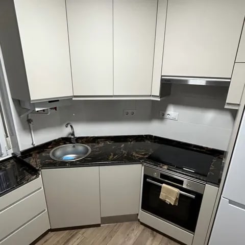 Cocina en esquina con mobiliario de carpintería blanco y encimera oscura veteada